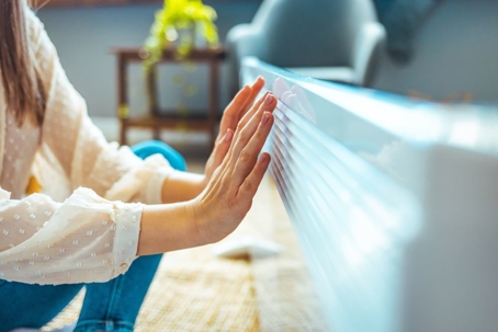 Woman warming her hands sitting by heater